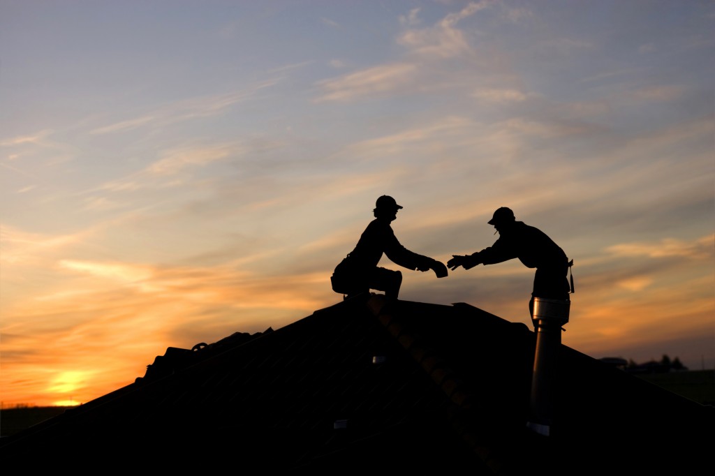 Two roofers working on roof at dusk